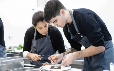 Dos aprendices de cocina, concentrados en emplatar un plato, aprendiendo como ser chef.