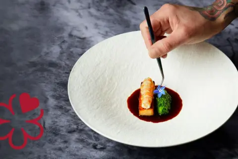 Un chef 3 estrellas Michelin decora un plato con langosta, brócoli y una flor azul.