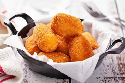 Croquetas doradas y crujientes en una sartén negra, listas para disfrutar.