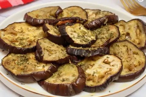 Rodajas de berenjena asada, tiernas y doradas, espolvoreadas con hierbas aromáticas. Un plato sencillo y delicioso para disfrutar del sabor de las berenjenas.