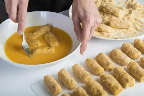 Manos rebozando croquetas en huevo. Se puede congelar la masa de croquetas para freír después.