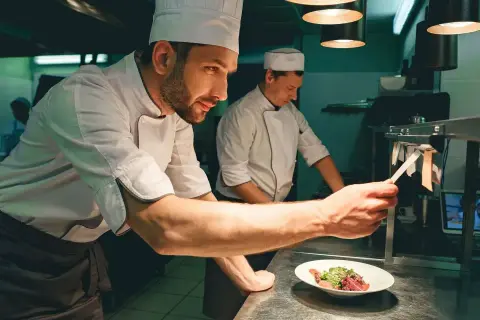 Un chef de partie, con su equipo, supervisa la preparación de un plato en una cocina profesional.