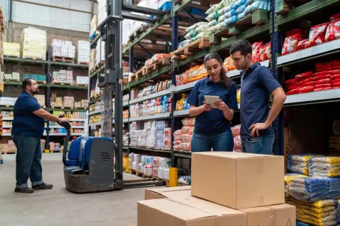 Trabajadores en un almacén revisan inventario en una tablet, gestionando el **cash and carry que es** un modelo de negocio eficiente.