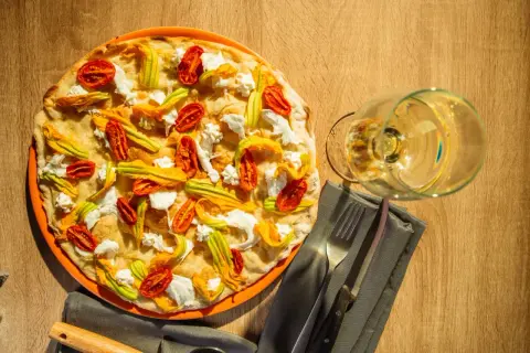 Deliciosa pizza tonda romana con flores de calabacín, tomates secos y ricotta. Un placer para la vista y el paladar.