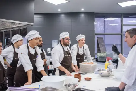 Chef instructor enseña a estudiantes a master food and beverage en una cocina profesional.