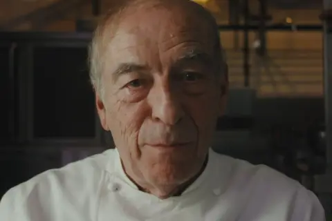 Retrato de un chef catalán con varias estrellas Michelin, con su uniforme blanco y mirada serena.