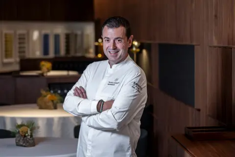 Chef sonriente en su cocina, con el logo de Ricard Camarena Restaurantes en su uniforme.