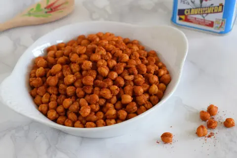 Un tazón blanco lleno de garbanzos fritos crujientes, sazonados con especias rojizas.