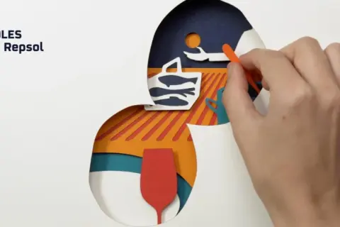 Guía Repsol: cómo conseguir un solete. Mano colocando piezas de papel recortado: cesta con peces, copa y sol.