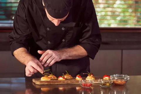 Chef en uniforme negro prepara canapés con salmón y alcaparras. Cada detalle cuenta en este arte de metre de cocina.