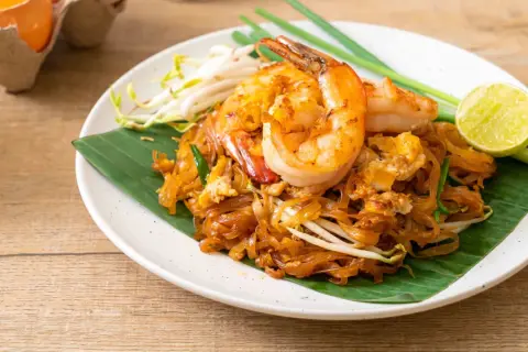 Pad Thai con camarones, perfecto para tu curso de cocina tailandesa. Servido sobre hoja de plátano, con brotes de soja, cebolleta y limón.