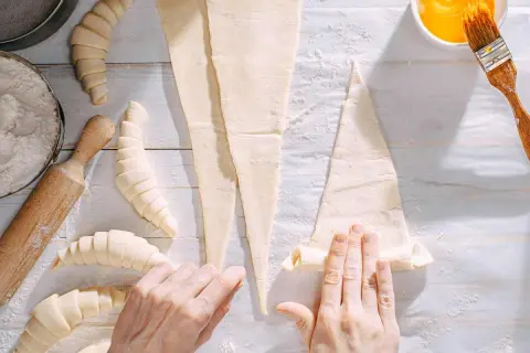 Manos enrollando masa para croissants. ¡Se pueden congelar los croissants para hornearlos más tarde!