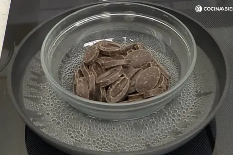 Chocolate troceado derritiéndose suavemente en un bol de cristal sobre un baño maría hirviendo.