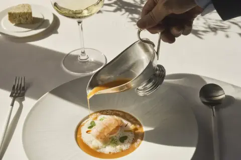 Servicio de sopa de marisco en un restaurante estrella Michelin. Un camarero vierte el caldo sobre un langostino y espuma.