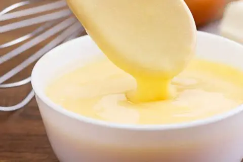 Crema pastelera cremosa cayendo de una cuchara a un bol. ¡Es bueno saber que se puede congelar la crema pastelera para usarla más tarde!