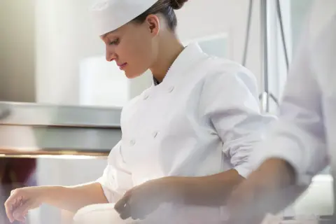 Chef concentrada en su labor, junto a otro chef en la cocina.