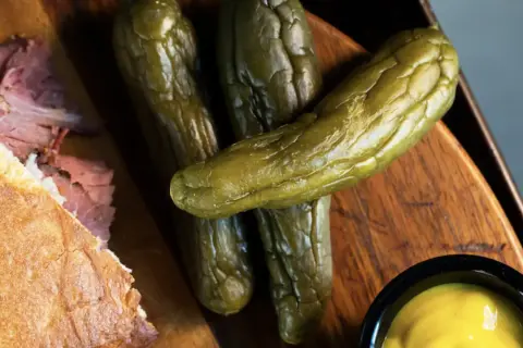 Un sándwich de pastrami como se come, con pepinillos y mostaza.