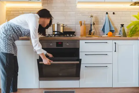 Mujer abre horno para cocinar al vapor en horno convencional.