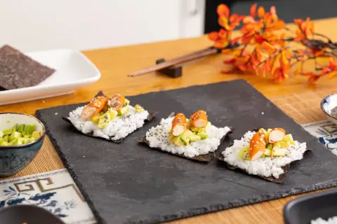 Tres pequeños rollos de sushi en proceso, listos para aprender a hacer sushi. Arroz, aguacate y palitos de cangrejo sobre alga nori.