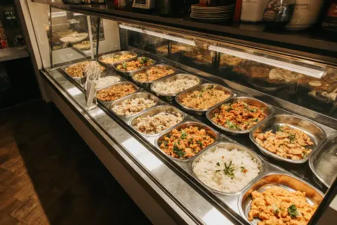Variedad de platos calientes en un negocio de comida para llevar. Arroz blanco, pollo y guisos apetitosos listos para servir.