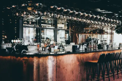 Barra de cobre pulido, botellas de licor, vasos y taburetes en este moderno bistro.