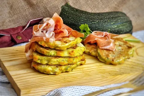 Deliciosas tortitas de calabacín apiladas y cubiertas con jamón serrano, listas para disfrutar.