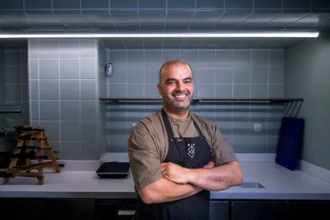 Chef sonriente con delantal negro en una cocina moderna, uno de los cocineros vascos famosos.