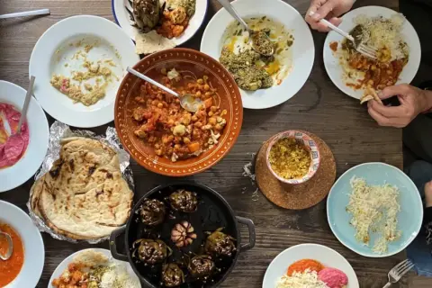 Mesa llena de platos variados, perfectos para recetas de cenas con amigos. Hummus, garbanzos, alcachofas y pan pita.