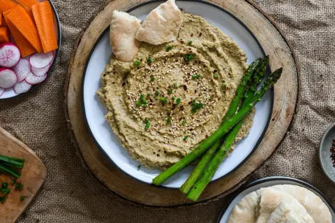 Hummus cremoso con espárragos, pan de pita y crudités de zanahoria y rábano. ¡Perfecto para tus ideas de picoteo saludables!