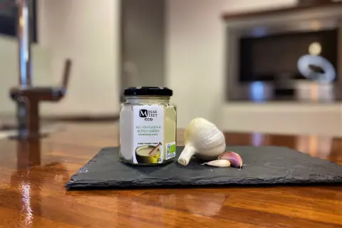 Tarro de alioli casero ecológico junto a una cabeza de ajo y dientes. ¡Este alioli se puede congelar para disfrutarlo más tiempo!