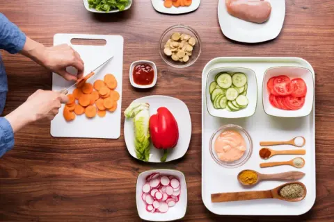 Mise en place restaurante: zanahorias cortadas, lechuga, pimiento rojo, pepino, tomate, pollo y condimentos listos para cocinar.