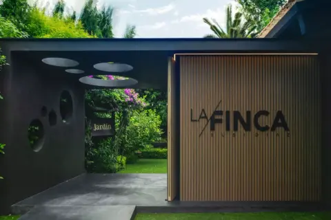 Entrada a "La Finca" de Susi Díaz, un jardín exuberante con un letrero de madera y una fachada moderna.