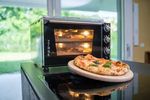 Horno eléctrico con dos pizzas dentro, una lista para disfrutar y otra en proceso. El tiempo de cocción de una pizza en horno eléctrico es clave para su textura.