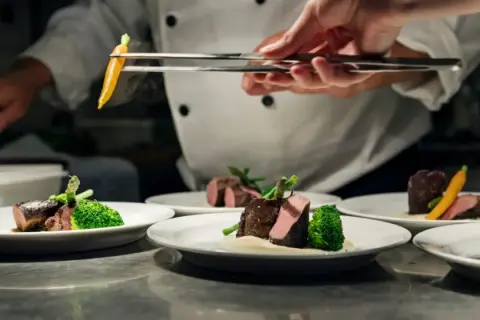 Chef emplata un plato de carne con brócoli y zanahoria, un detalle digno de una estrella verde Michelin.