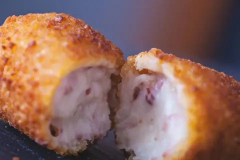 Croqueta dorada y crujiente, partida por la mitad, revelando un interior cremoso. La proporción de harina y leche para croquetas es clave para esta textura.