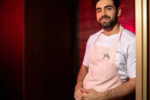 Chef Serrano, parte de la lista cocineros estrellas Michelin, sonríe con delantal rosa.