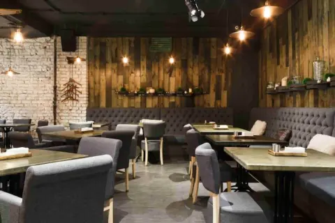 Interior de un restaurante de un tenedor con mesas de madera, sillas tapizadas y paredes de ladrillo y madera.