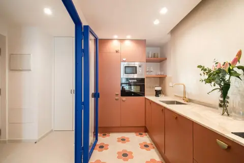 Cocina moderna con armarios naranjas, encimera de mármol y suelo hexagonal. Perfecta para un curso intensivo de cocina.