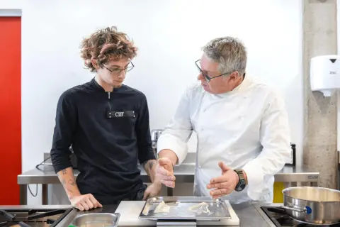 Un chef experimentado enseña a un joven aprendiz, mostrando diferentes tipos de chef en acción en una cocina profesional.