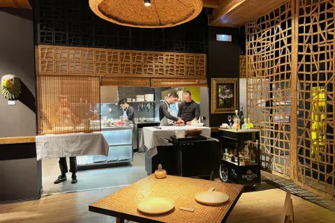 Chefs trabajan en la cocina de un restaurante. Se ve una mesa puesta y un carrito de bebidas. ¡Qué ganas de comer como Paco Méndez!