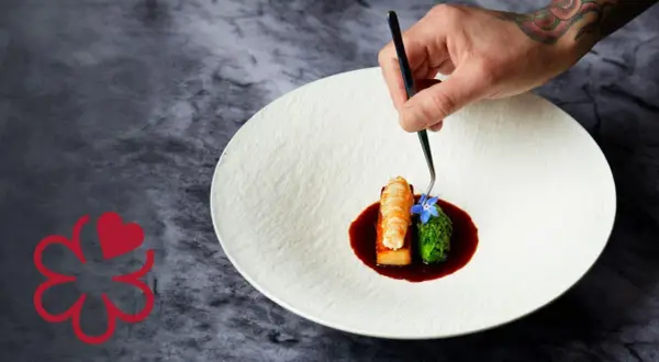 Un chef 3 estrellas Michelin decora un plato con langosta, brócoli y una flor azul.