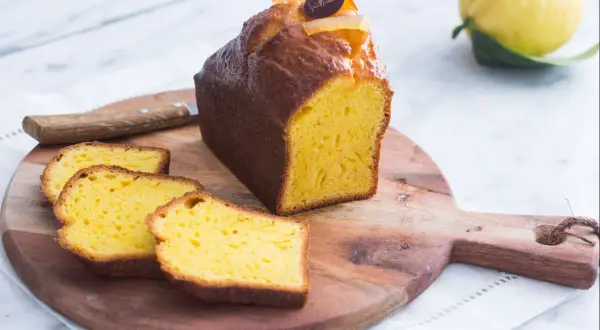 Un delicioso plumcake de limón, recién cortado, con rodajas esponjosas y un limón fresco al fondo.