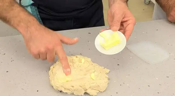 Man integrando mantequilla a la masa, un paso clave en la autolisis para un pan perfecto.