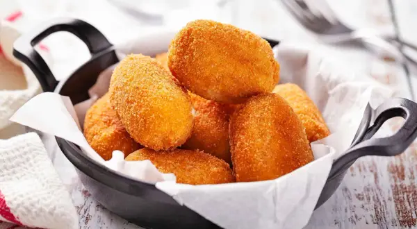 Croquetas doradas y crujientes en una sartén negra, listas para disfrutar.