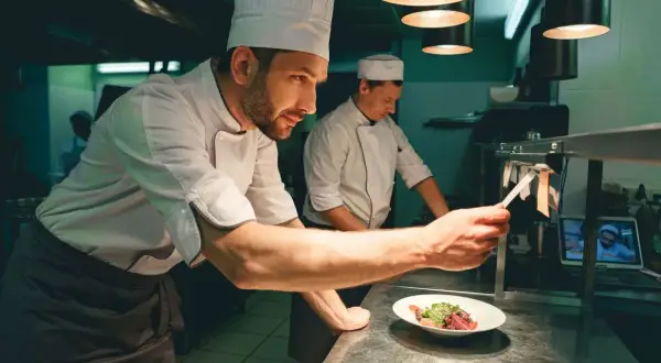 Un chef de partie, con su equipo, supervisa la preparación de un plato en una cocina profesional.