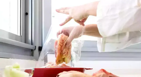 Manos con guantes introducen pollo en una bolsa para cocina al vacío.