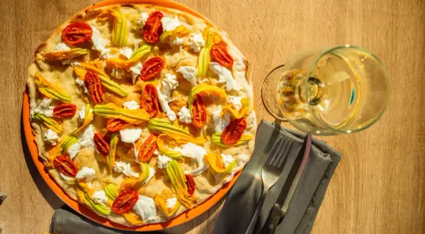 Deliciosa pizza tonda romana con flores de calabacín, tomates secos y ricotta. Un placer para la vista y el paladar.