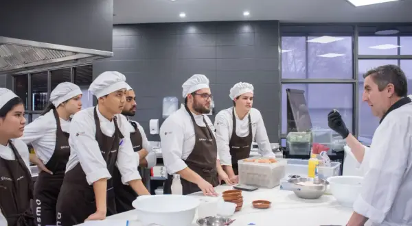 Chef instructor enseña a estudiantes a master food and beverage en una cocina profesional.