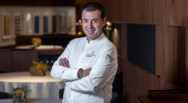 Chef sonriente en su cocina, con el logo de Ricard Camarena Restaurantes en su uniforme.
