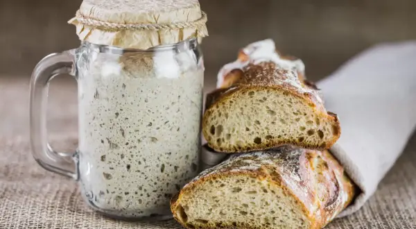 Masa madre burbujeante en un frasco junto a pan recién horneado. La clave para un buen pan está en el tiempo y temperatura para hornear pan.
